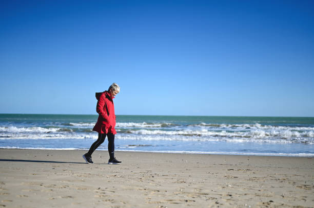 istock senior woman walking alone on a stormy beach. 1777985078
