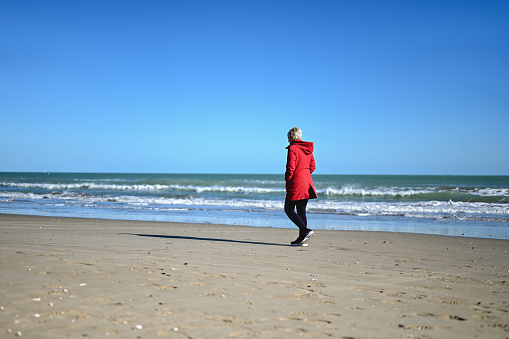 rear view of a mature woman walking on a beach in a cold weather.