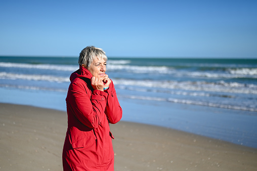 portrait of a gray haired woman walking alone on the beach in a windy weather.