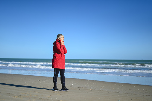 Senior woman in a red coat on a winter beach.