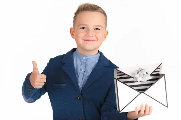Stylish and smiling caucasian young boy with gift box similar to a mail or present for christmas.Boy shows thumbs up. Isolated white background.