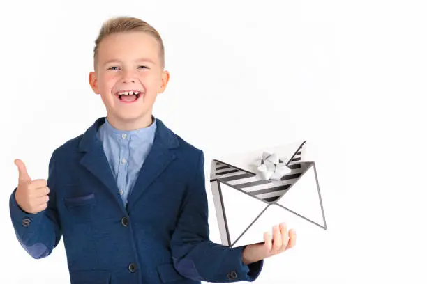 Stylish and smiling caucasian young boy with gift box similar to a mail or present for christmas.Boy shows thumbs up. Isolated white background.