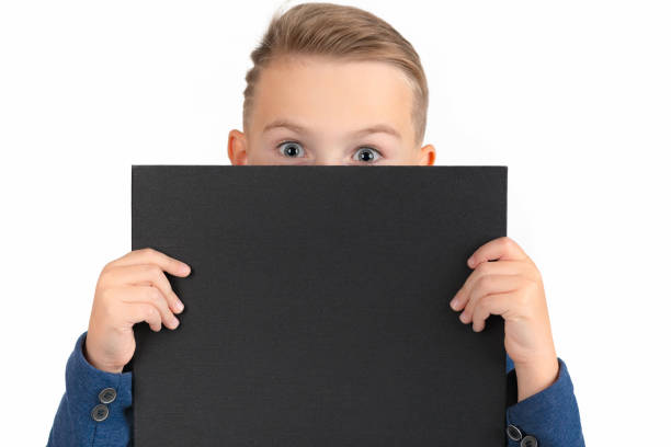 istock caucasian boy covers himself with blank poster, only eyes are visible. boy displaying blank black board for your text 1777989610