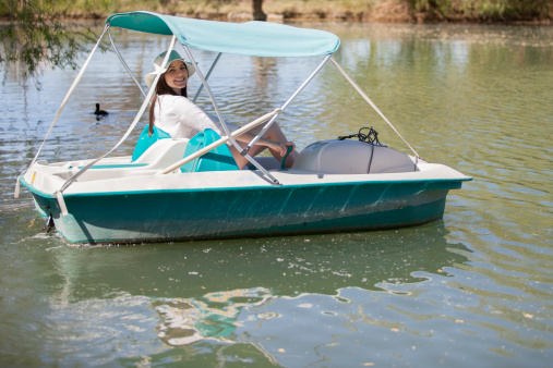 Cute happy girl taking a ride in a pedal boat on a sunny day at a lake