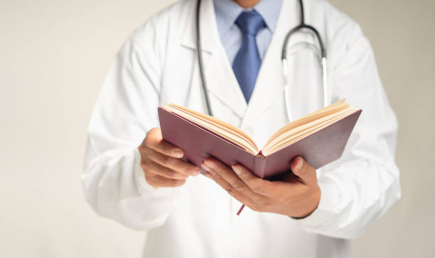 istock Doctor in a uniform reading a book while standing against a gray background 1778007160