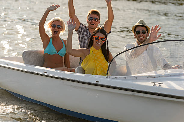 Waving young people in sunglasses sitting in motorboat summertime