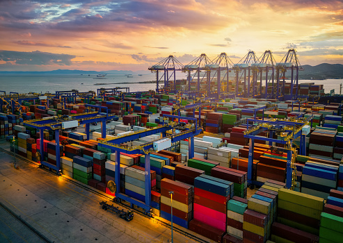 Aerial view of a commercial port with stacks of containers and loading cranes during sunset time