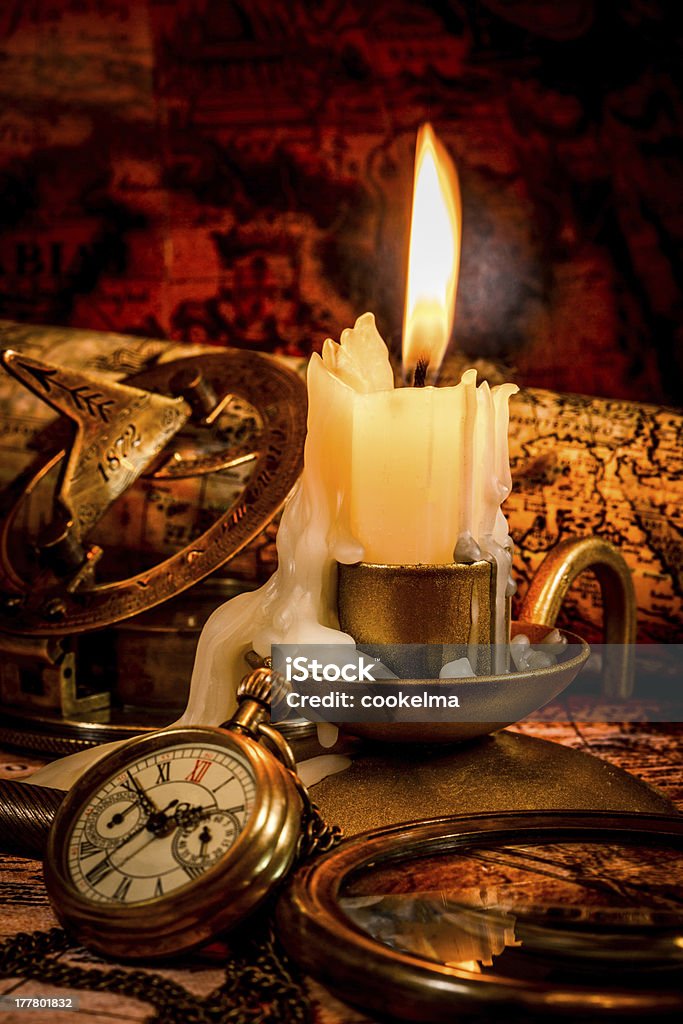 Vintage items on ancient map. Vintage compass, pocket watch lie on an old ancient map with a lit candle Abstract Stock Photo