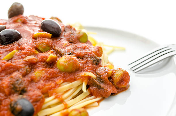 Detail of spaghetti with tomato sauce, olives and capers on a white plate.