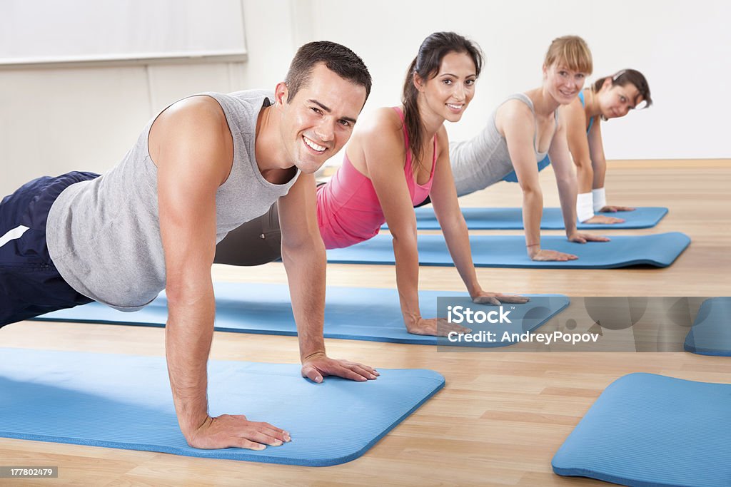Gym class doing press ups Group of diverse healthy people in a gym class doing press ups while exercising on two rows of blue mats on a wooden floor Active Lifestyle Stock Photo