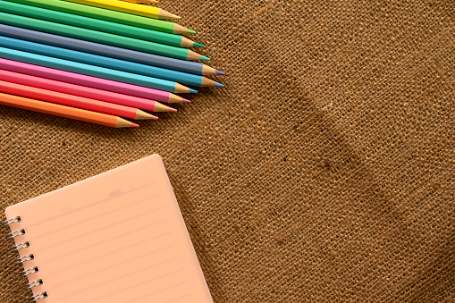 Colored pencils pastel and notebooks lay on brown crumpled burlap.