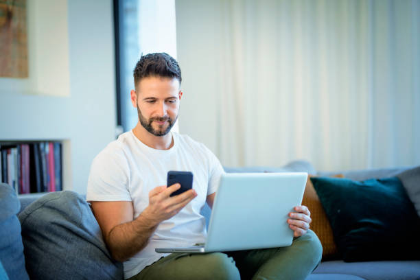 istock Handsome man sitting at home and using a laptop and mobile phone for work 1778045363