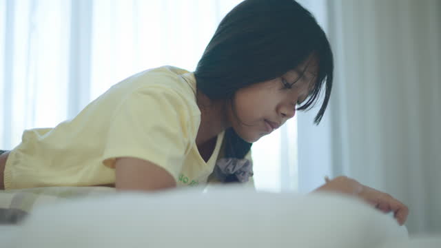Teenage girl lying on front on her bed doing homework.