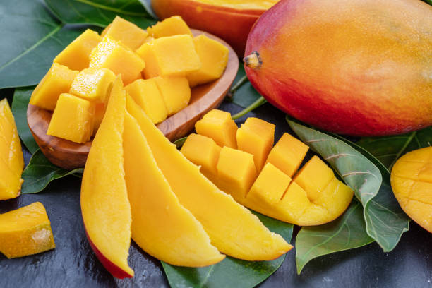 istock Ripe mango fruits with slices and mango leaves on a gray stone table. Nice fruit background for your projects. 1778058075