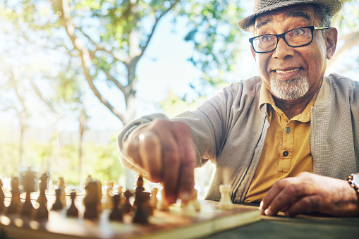 Elderly man in park, hand and chess game strategy, competition or challenge, retirement and moving piece. Closeup, planning and contest outdoor, concentration on boardgame and recreation in nature