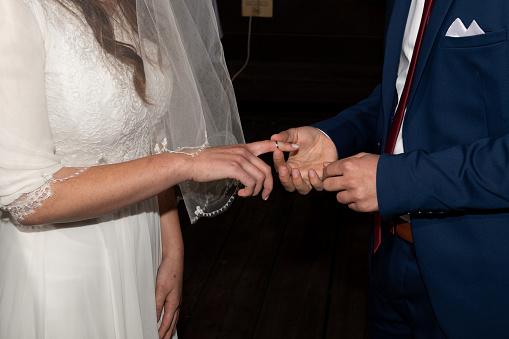 A bride extends her hand and finger to receive the ring purchased by the groom during a Jewish wedding ceremony.