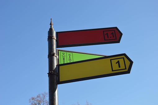 A pillar with colored direction arrows and destination numbers against the sky. Metal street sign. Place for names.
