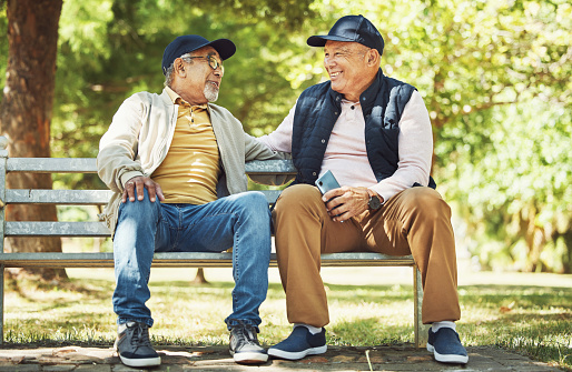 Senior friends, smile and relax on park bench, talking and bonding outdoor in retirement. Happy elderly men sitting together in garden, communication and chat in nature in the morning with phone.