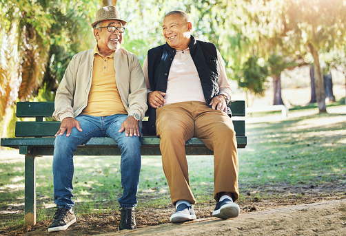 Senior friends, men and smile at park bench, talking and bonding outdoor to relax. Happy elderly people sitting together in garden, communication and conversation in nature for retirement in spring
