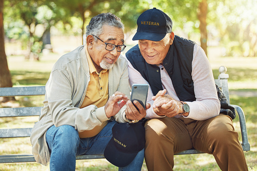 Elderly men, friends and phone in park, reading and army memory with thinking, relax and sunshine. Senior military veteran, smartphone and talk on bench, nostalgia and remember service in global war