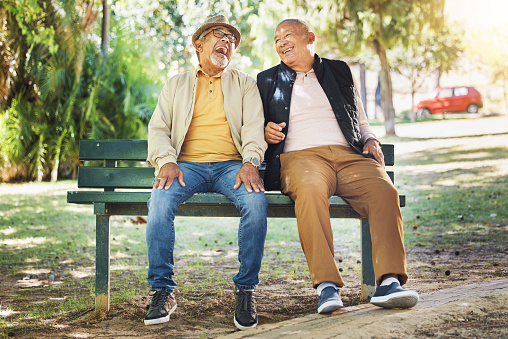 Elderly friends, happy and men on park bench, talking and bonding outdoor to relax in retirement. Funny senior people sitting together in garden, communication and laughing at joke, comedy and smile