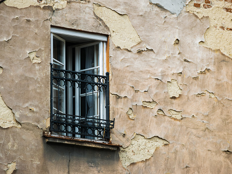 An open window with a metal grill on an old wall with peeling plaster