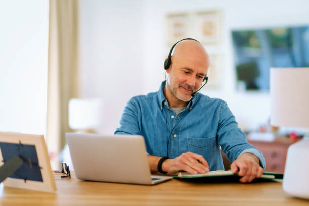 istock Mid aged man with headset sitting at home and using laptop 1778107055