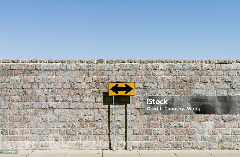 Road sign with double arrows Road sign marked as double arrows, over brick wall and blue sky, Two Objects Stock Photo