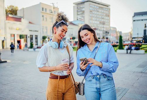 Young cheerful women friends looking at a mobile phone in the city