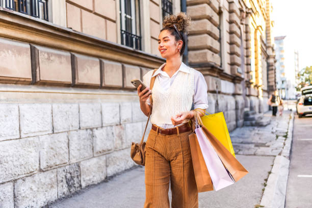 Woman using a mobile phone and carrying shopping bags Young cheerful woman using mobile phone and carrying shopping bag while shopping in the city mall walker stock pictures, royalty-free photos & images