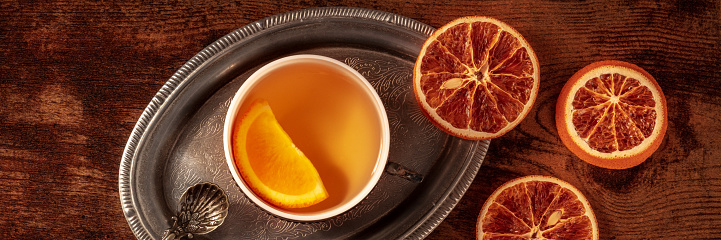 Orange tea with fresh and dried oranges panorama, a cup on a vintage tray on a dark rustic wooden background, overhead flat lay shot