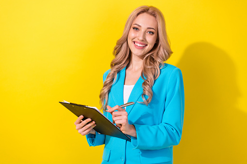 Portrait of positive successful person toothy smile hold clipboard documents pen isolated on yellow color background.