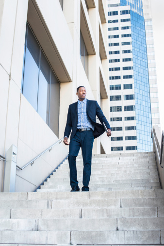 A young handsome black businessman is walking down on steps from a business building.