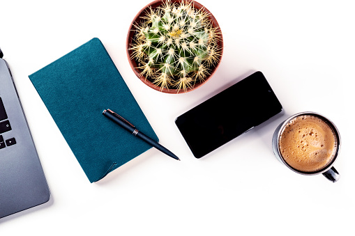 Desk, top view on a white background. Coffee, notebook, phone, plant, and laptop, overhead flat lay shot. Work layout