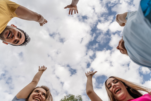Low angle view of group of friends raising hands while standing against cloudy sky