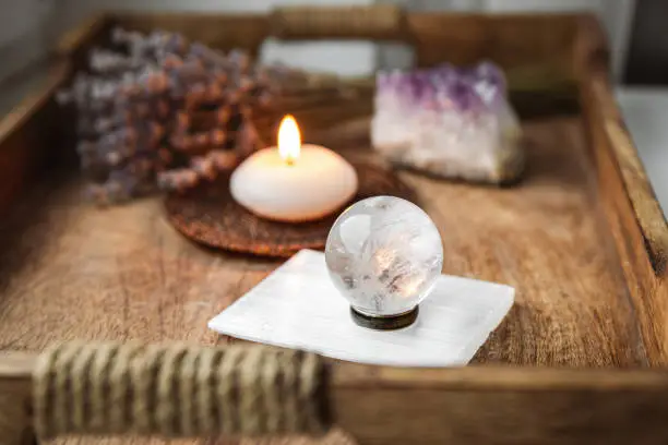Gemstone sphere or crystal balls known as crystallum orbis and orbuculum which is the beacon of peace and harmony in home environment. Natural clear quartz ball on stand on wood tray in home.