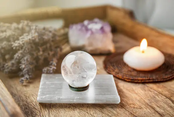 Gemstone sphere or crystal balls known as crystallum orbis and orbuculum which is the beacon of peace and harmony in home environment. Natural clear quartz ball on stand on wood tray in home.