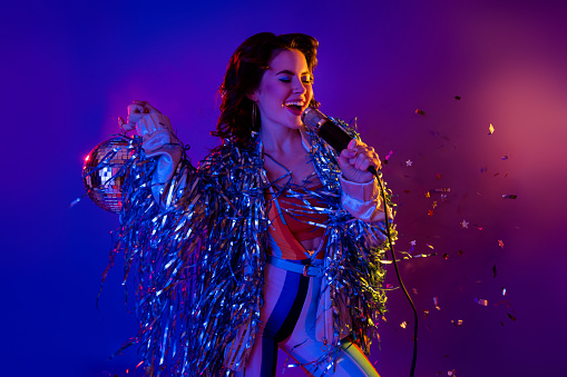 Photo of pretty cool lady wear tinsel jacket rising discoball singing songs isolated neon purple color background.