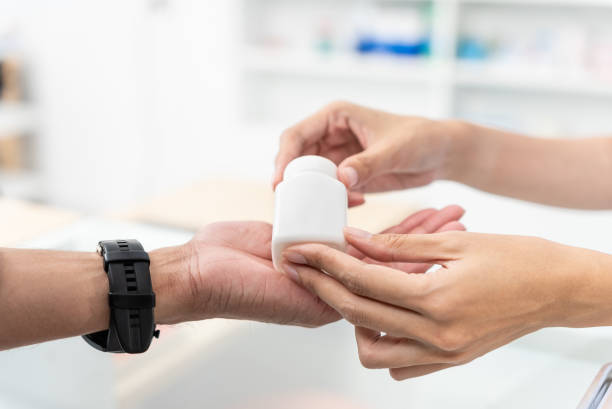 cierre las manos de la farmacéutica vendedora y el cliente masculino que compra medicamentos en la farmacia, entregue el frasco de píldoras de medicina de la mano a otra carga de mano. - opening bottle pill bottle pill fotografías e imágenes de stock