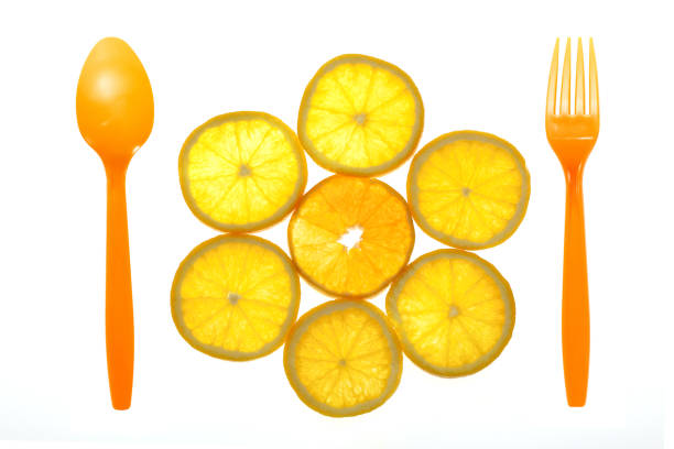 Slice of orange fruit with orange fork and spoon isolated on white background from top view.