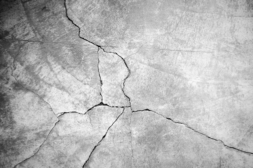 A gray weathered, dirty concrete wall with a large crack running down it.