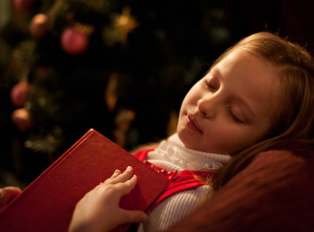 girl sleeping near Christmas tree. Book is in her hand stock photo