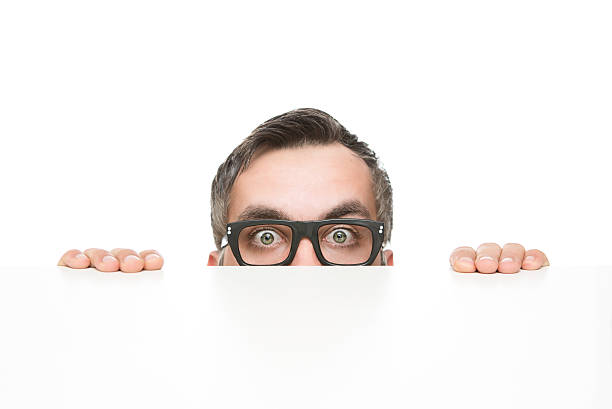 Funny nerd peeking Funny nerd peeking from behind the desk isolated on white background with copy space nerd stock pictures, royalty-free photos & images