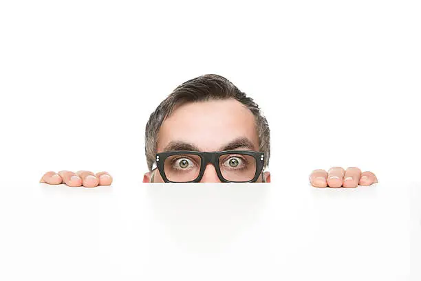 Funny nerd peeking from behind the desk isolated on white background with copy space