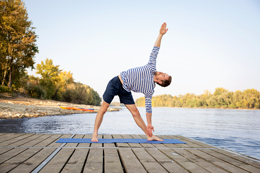 Mid aged man practicing yoga outdoor. Caucasian man using yoga mat and doing yoga on nature.