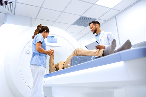Female doctor assisting senior patient while doing MRI scan in medical examination room