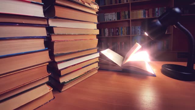 Book on desk in library at lamp, wind turning pages, books, bookshelves and globe on background