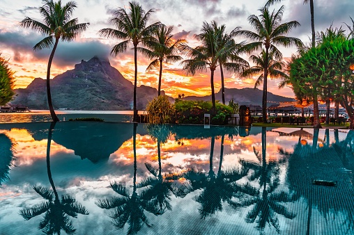 A beautiful sunrise over a pool with palm trees and mountains in the background. Bora Bora