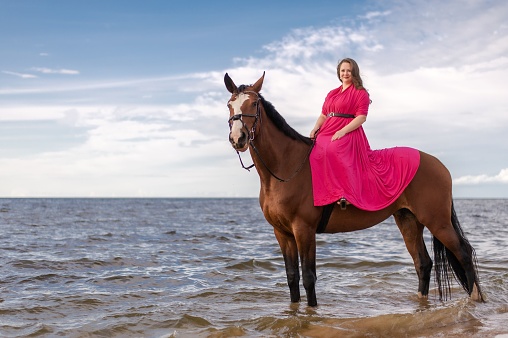 A woman in a vibrant dress galloping on a majestic white horse through the refreshing waters of a lake or river
