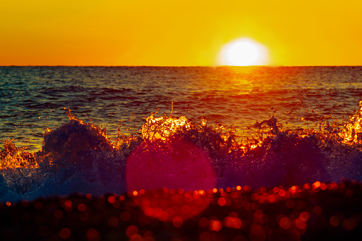 Sunset on sea. Sun sets behind horizon of sea. Splash of waves. Sunset landscape.